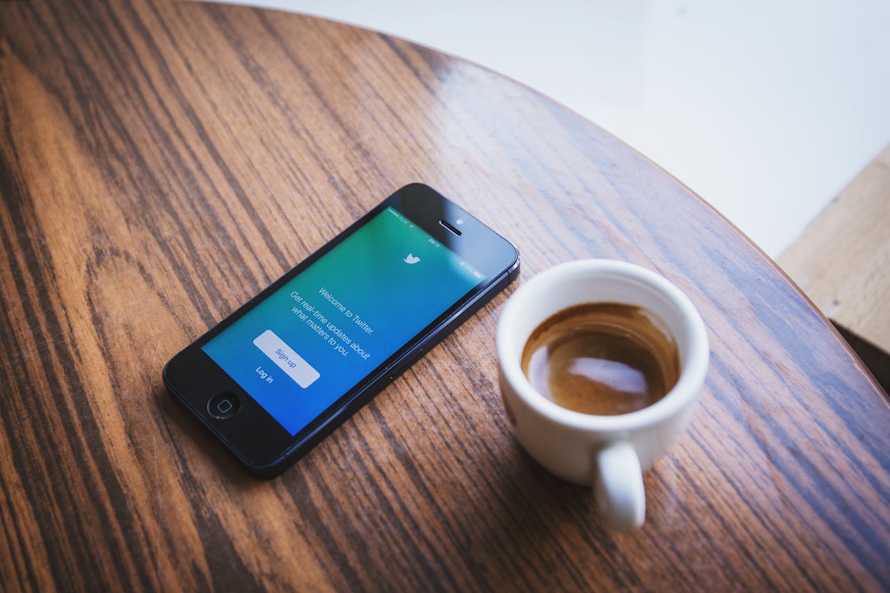 Crafting Captivating Headlines: Your awesome post title goes here Close-up of a smartphone with the Twitter app next to a cup of coffee on a wooden table.
