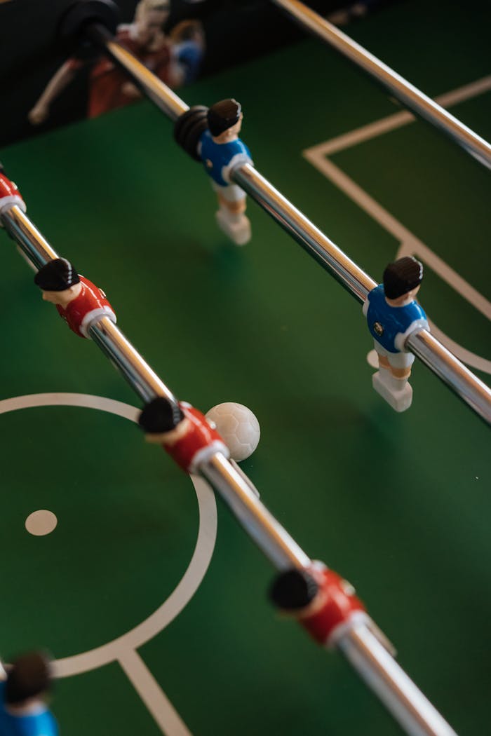 contact-img Dynamic foosball game action showing close-up of players and ball on a table.